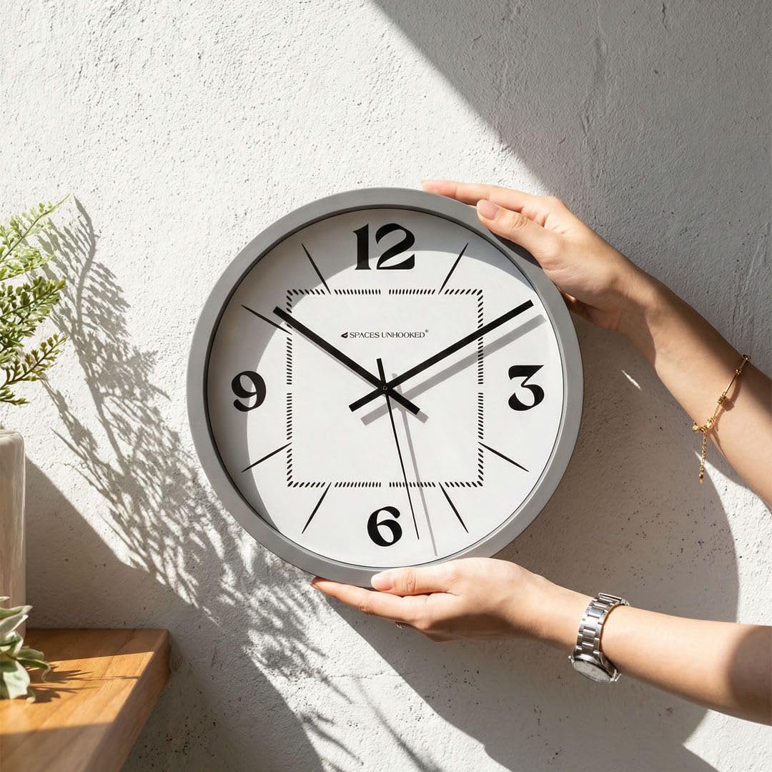Person holding a round wall clock against a light-colored wall.