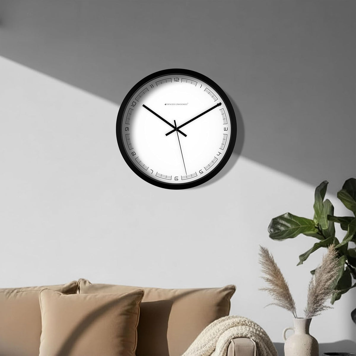 Wall clock on a gray wall with a neutral-colored sofa and decorative elements in the foreground