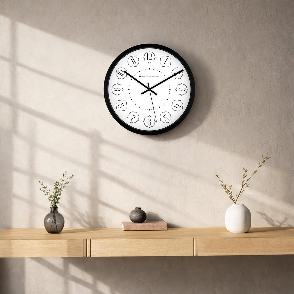 Wall clock on a wall with a wooden shelf below featuring decorative items.