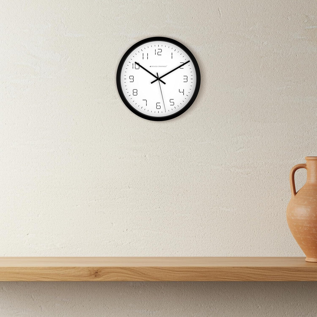 Wall clock on a plain wall with a wooden shelf and vase in the foreground