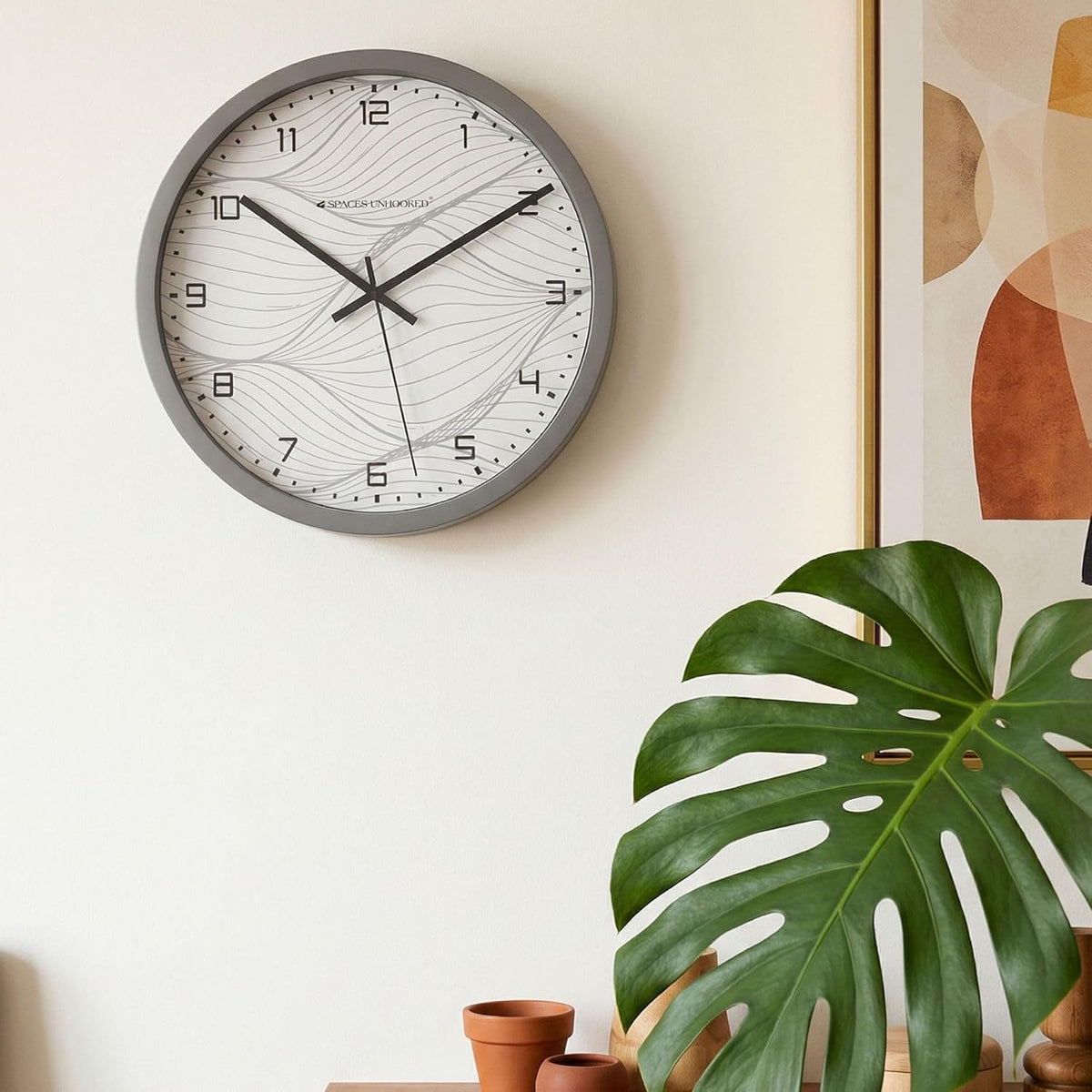 Wall clock on a wall with a plant and abstract art in the background
