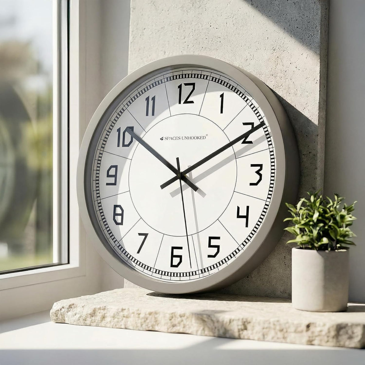 Wall clock on a ledge with a plant and window in the background