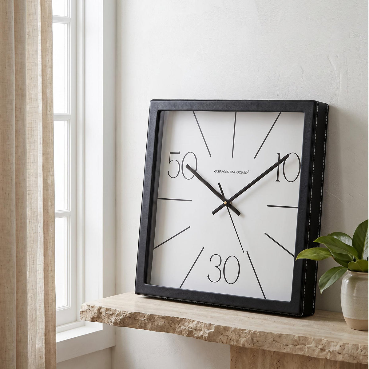 Square black wall clock with radial lines and numerals 10, 30, 50, front view