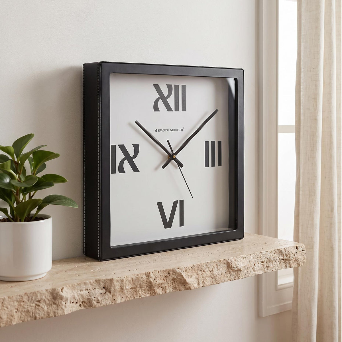 Square black wall clock with four bold Roman numerals on a plain white dial, front view