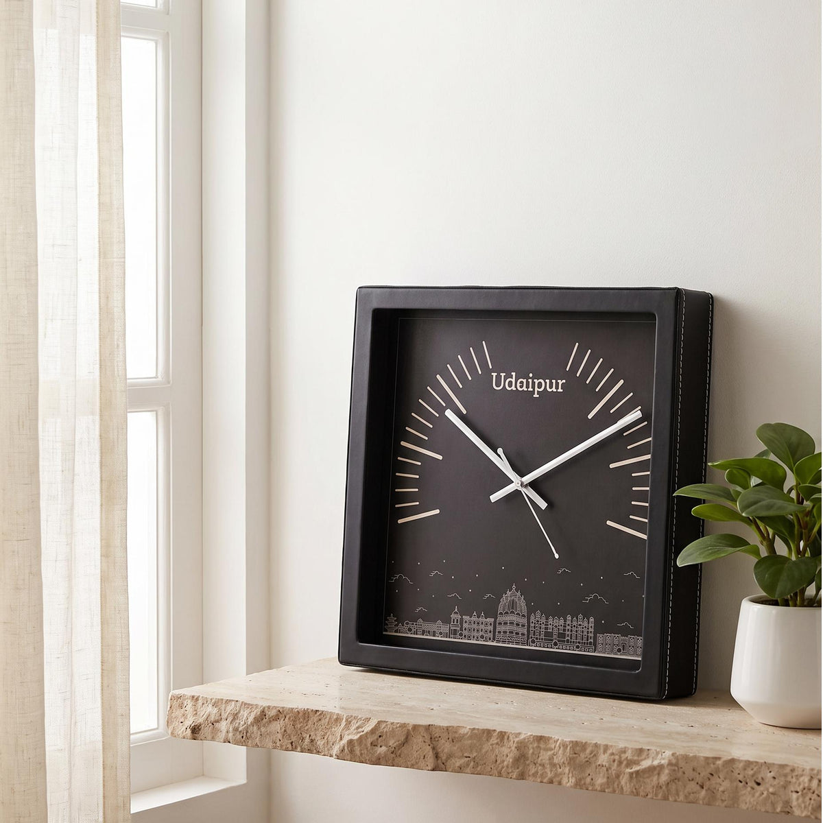 Black square wall clock with Udaipur skyline art and white markers, front view