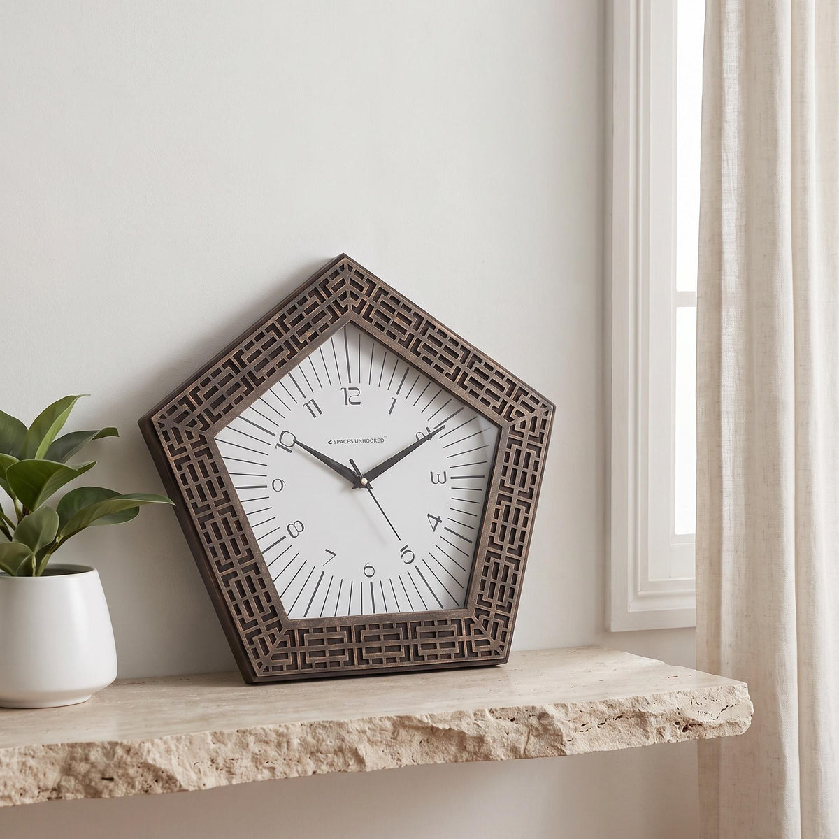 Pentagon wall clock with bronze maze-pattern frame and radiating lines on a white dial