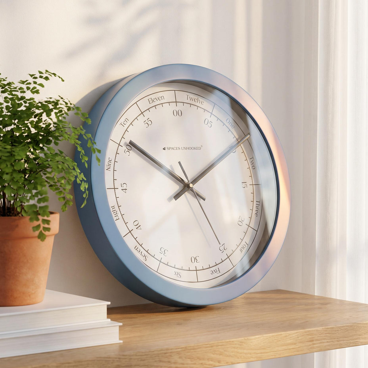 Spaces Unhooked blue round wall clock with hours written in words on a white dial, front view