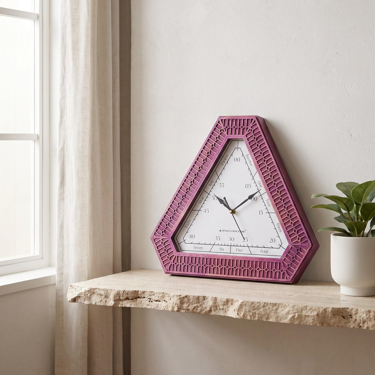 Triangular wall clock with magenta carved frame and word dial on white, front view