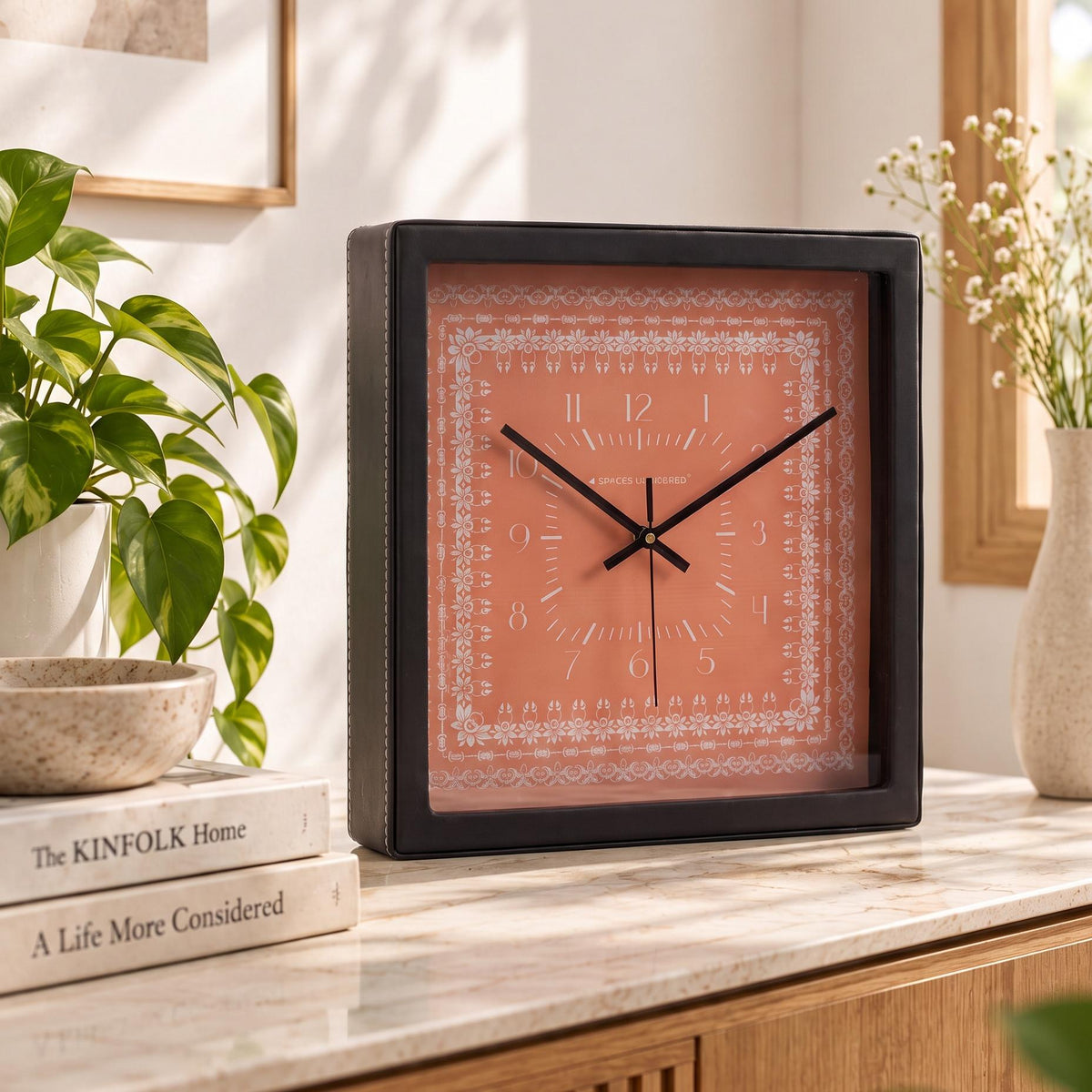 Square black wall clock with coral dial and white floral lace border, front view