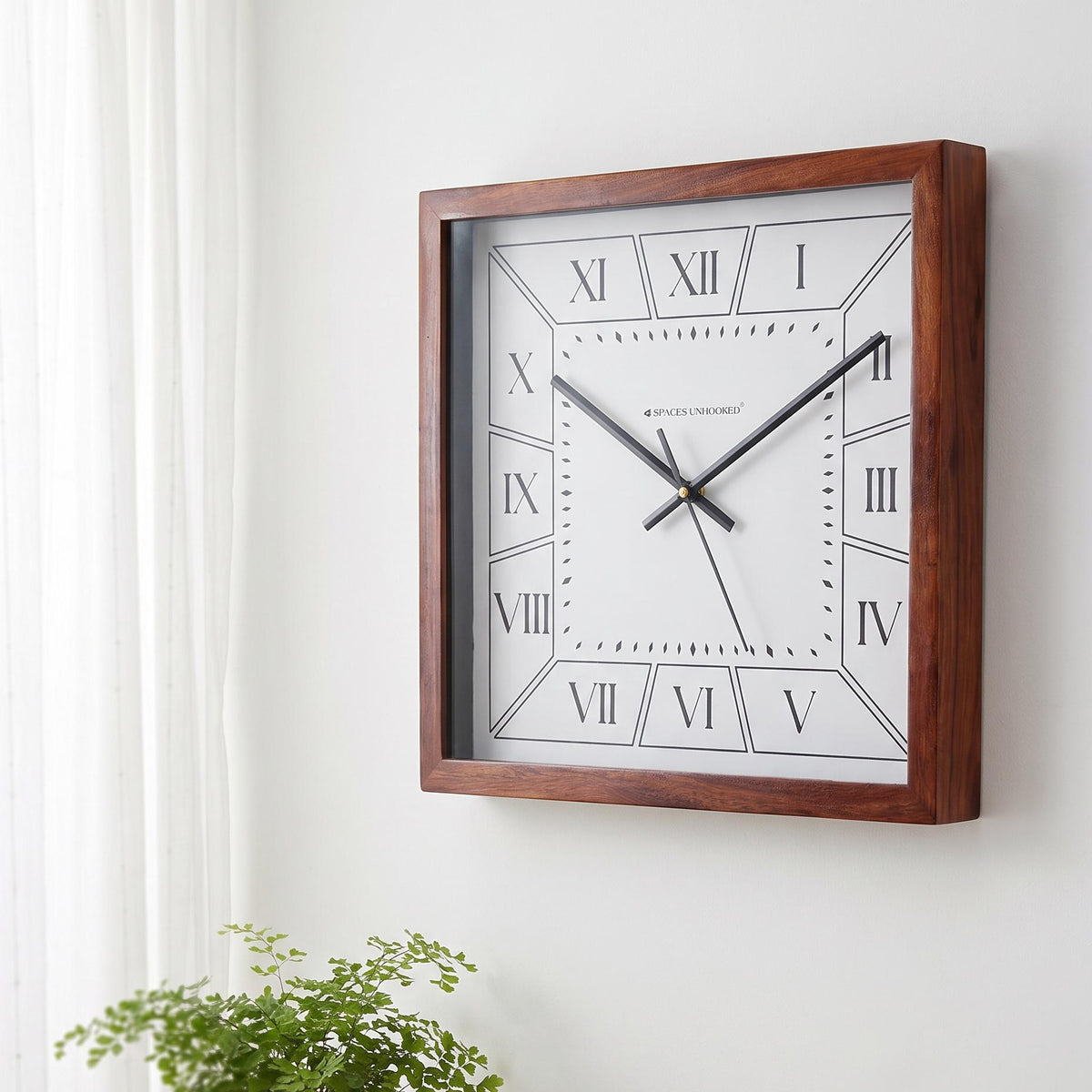 Roman numeral wall clock with brown frame on a hallway wall with framed art and brass accents