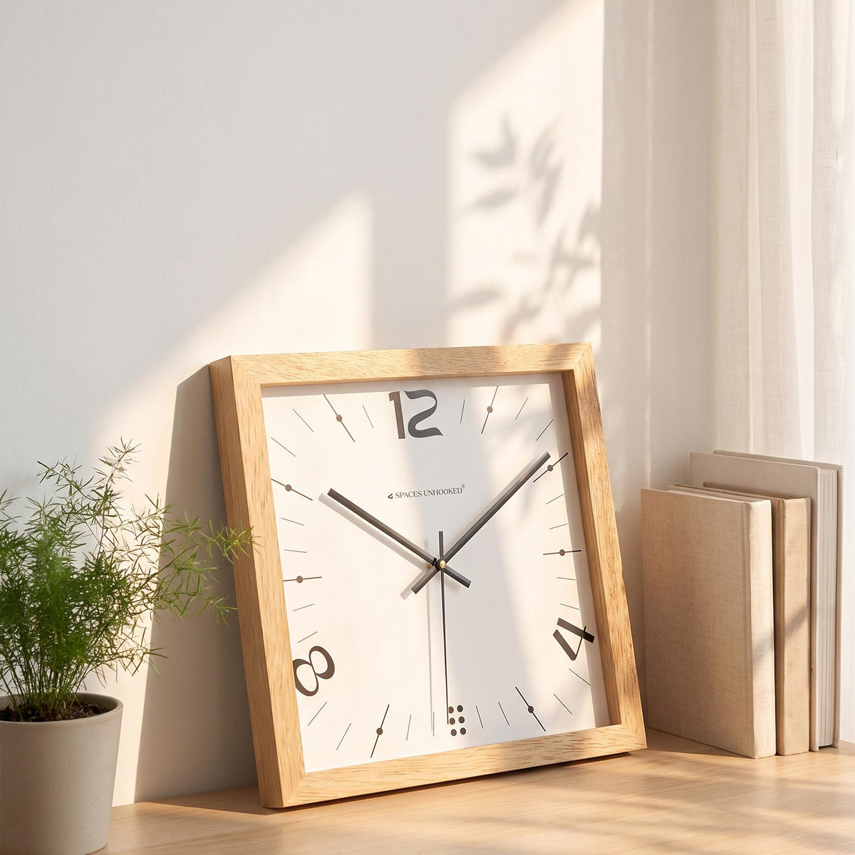 Black hands and thin second hand over the white dial of a light oak square wall clock