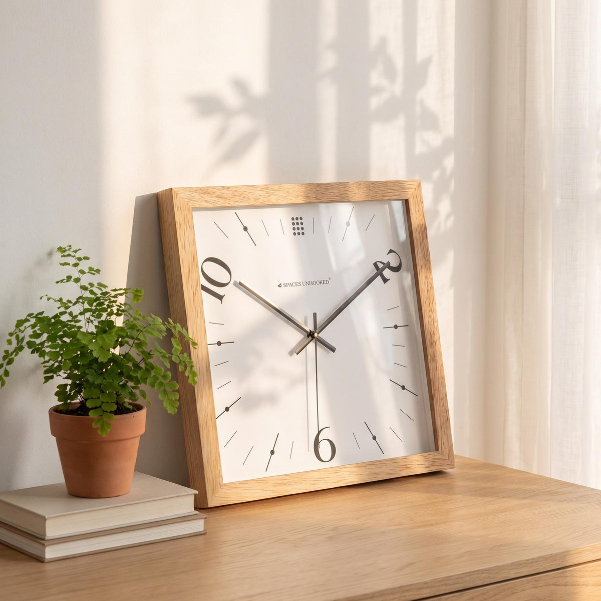 Black hands and thin second hand over the white dial of a light oak square wall clock