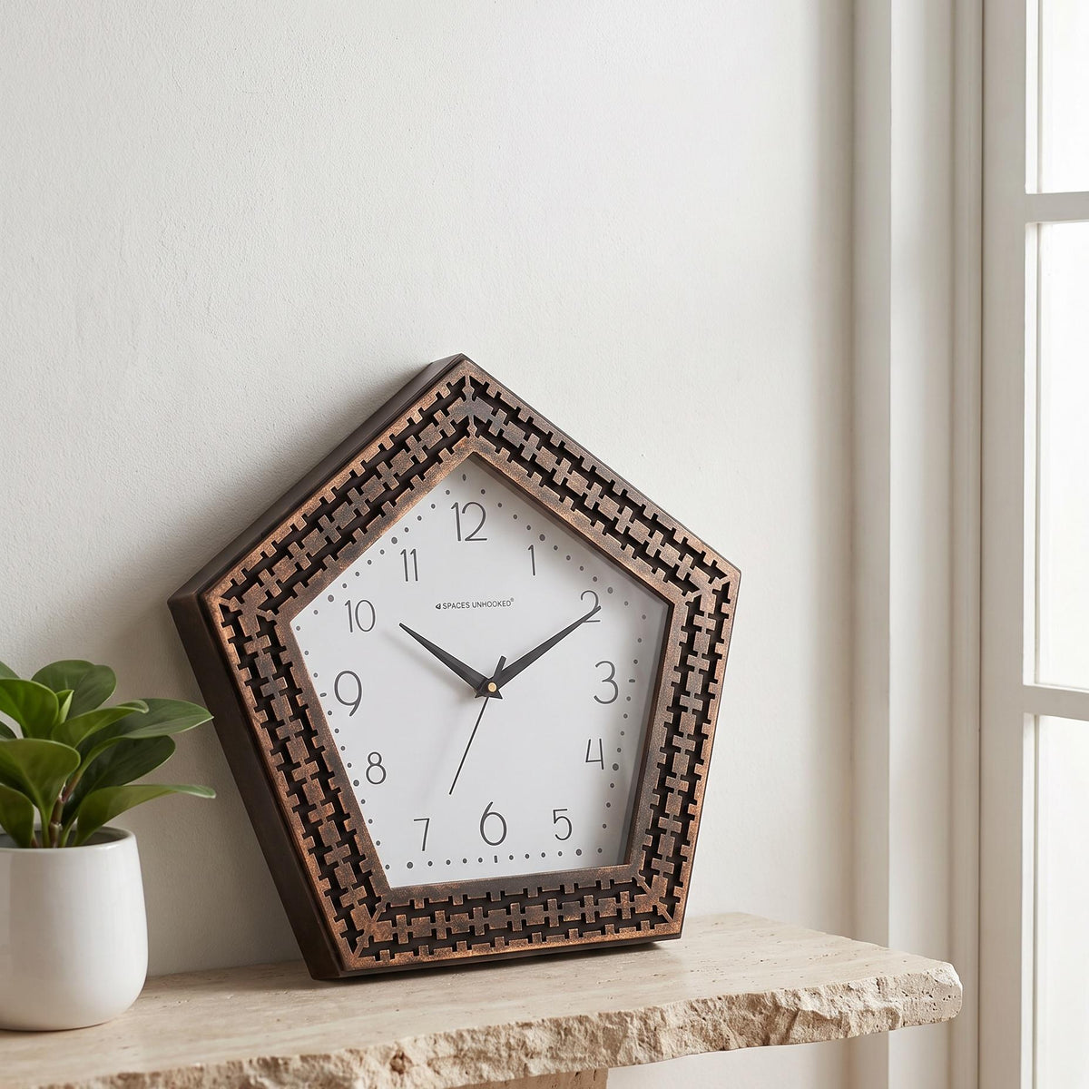 Pentagon wall clock with copper-finish woven frame and dotted dial on white, front view