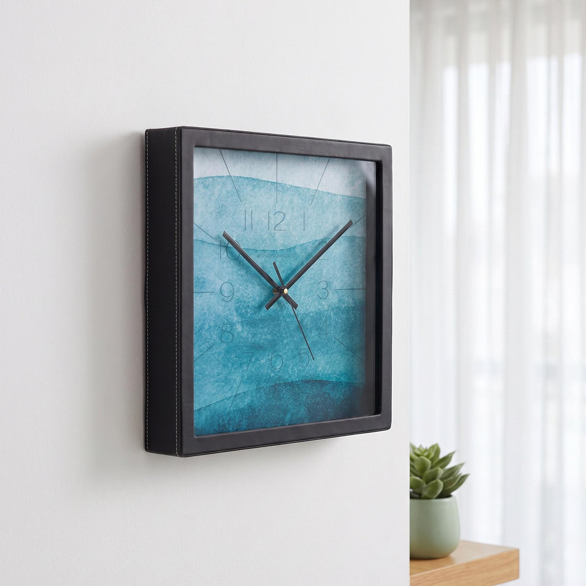 Teal watercolour wall clock on a dining room wall beside a window