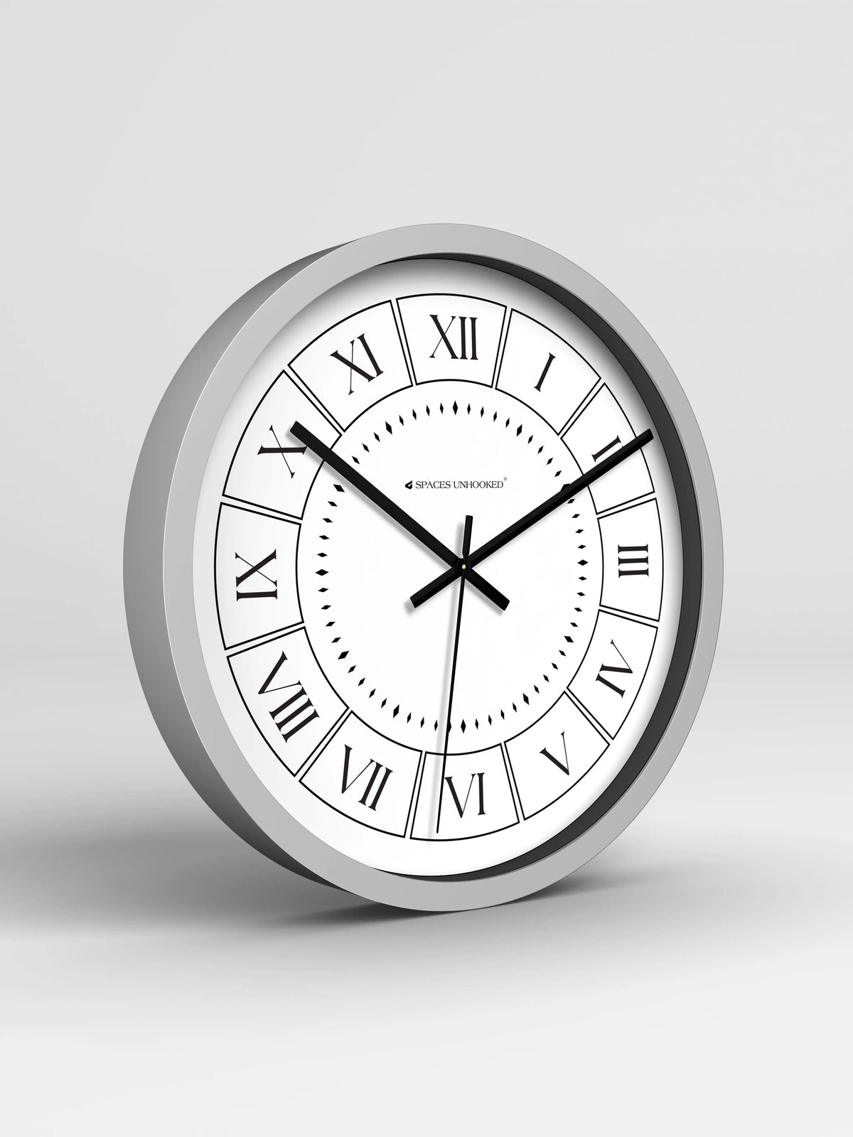 Gray-framed wall clock with Roman numerals on white face, displaying 10:11, mounted on beige wall above a potted plant and white vase.