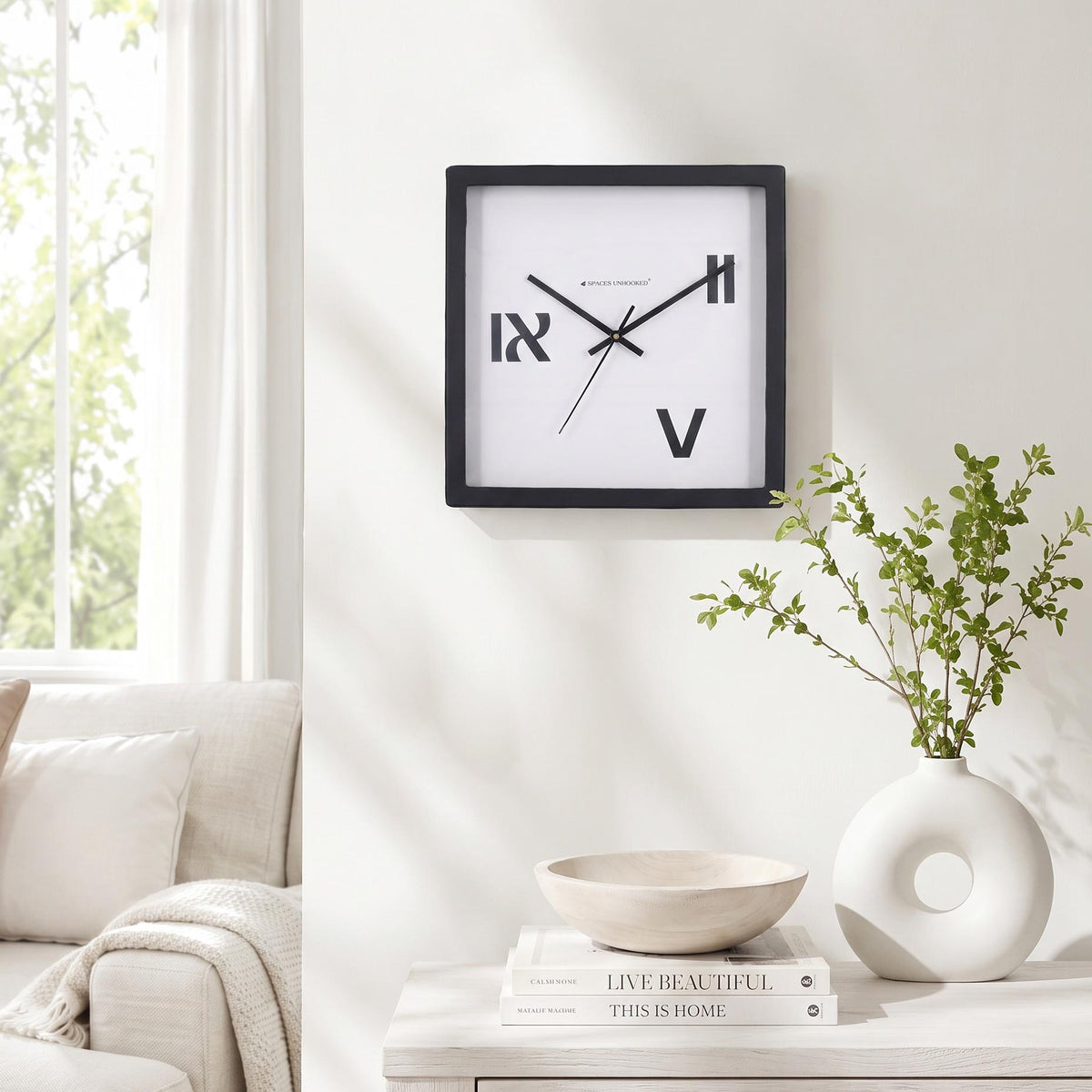 Three roman numeral wall clock on a hallway wall beside framed art