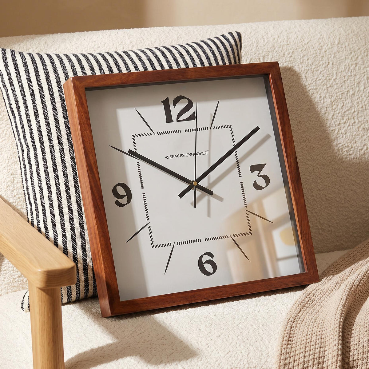 Slim black hands and fine second hand over the dotted centre of a square wooden wall clock