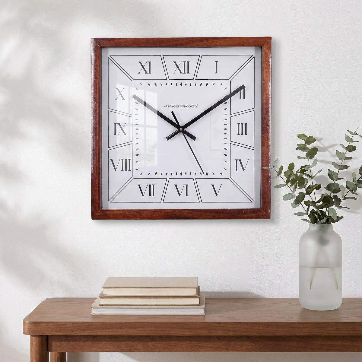 Slim black hands and thin second hand across the white dial of a Roman numeral wall clock