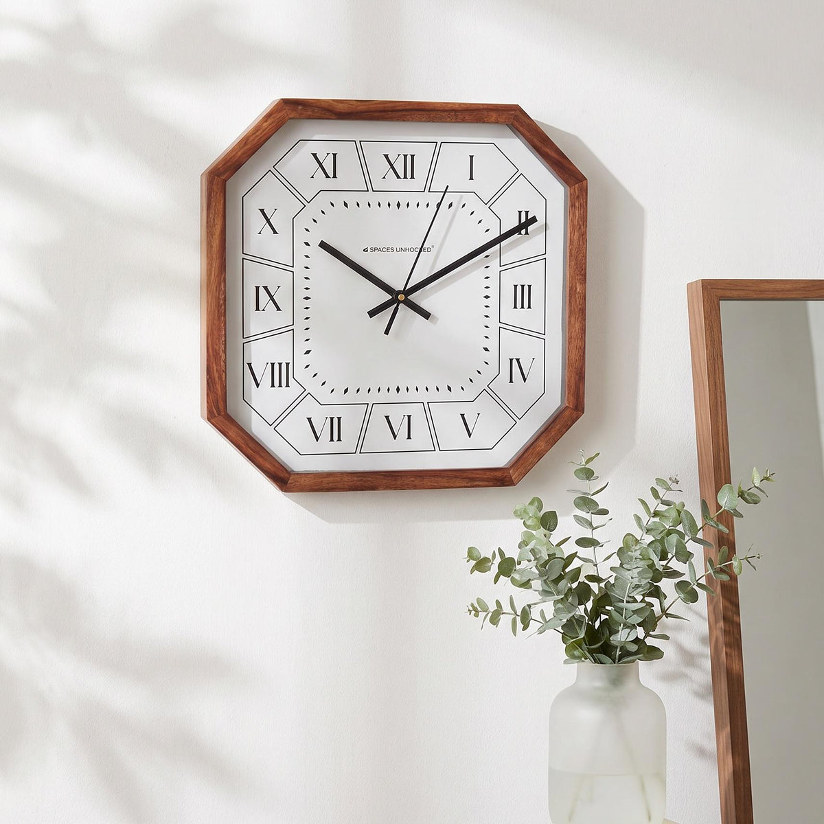 Slim black hands and thin second hand across the white dial of a Roman numeral wall clock