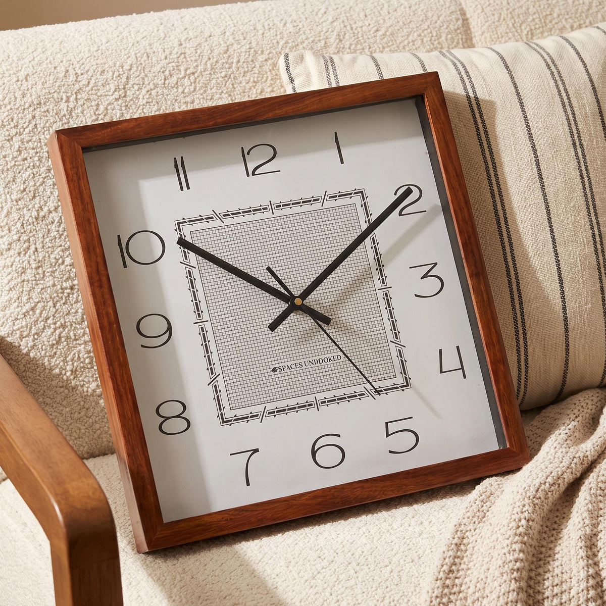 Slim black hands and thin second hand over the grid centre of a square wooden wall clock