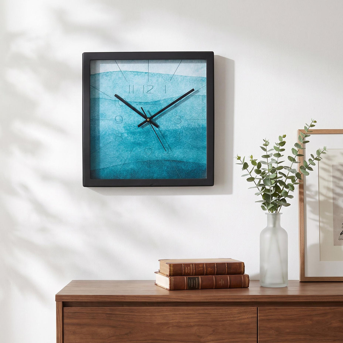 Spaces Unhooked logo above the brass-toned centre cap on a teal watercolour clock dial