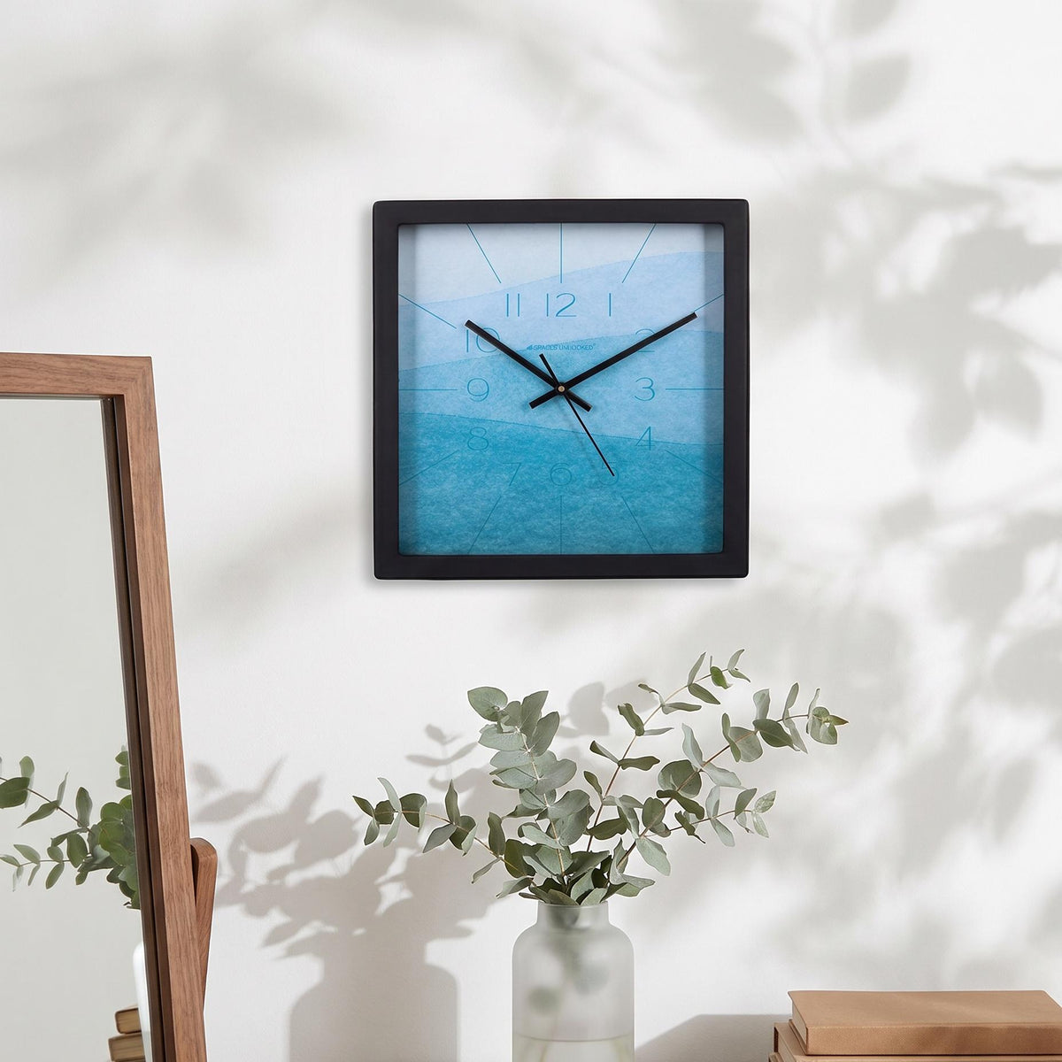 Black square frame and clear cover of a sky blue watercolour wall clock, close-up view