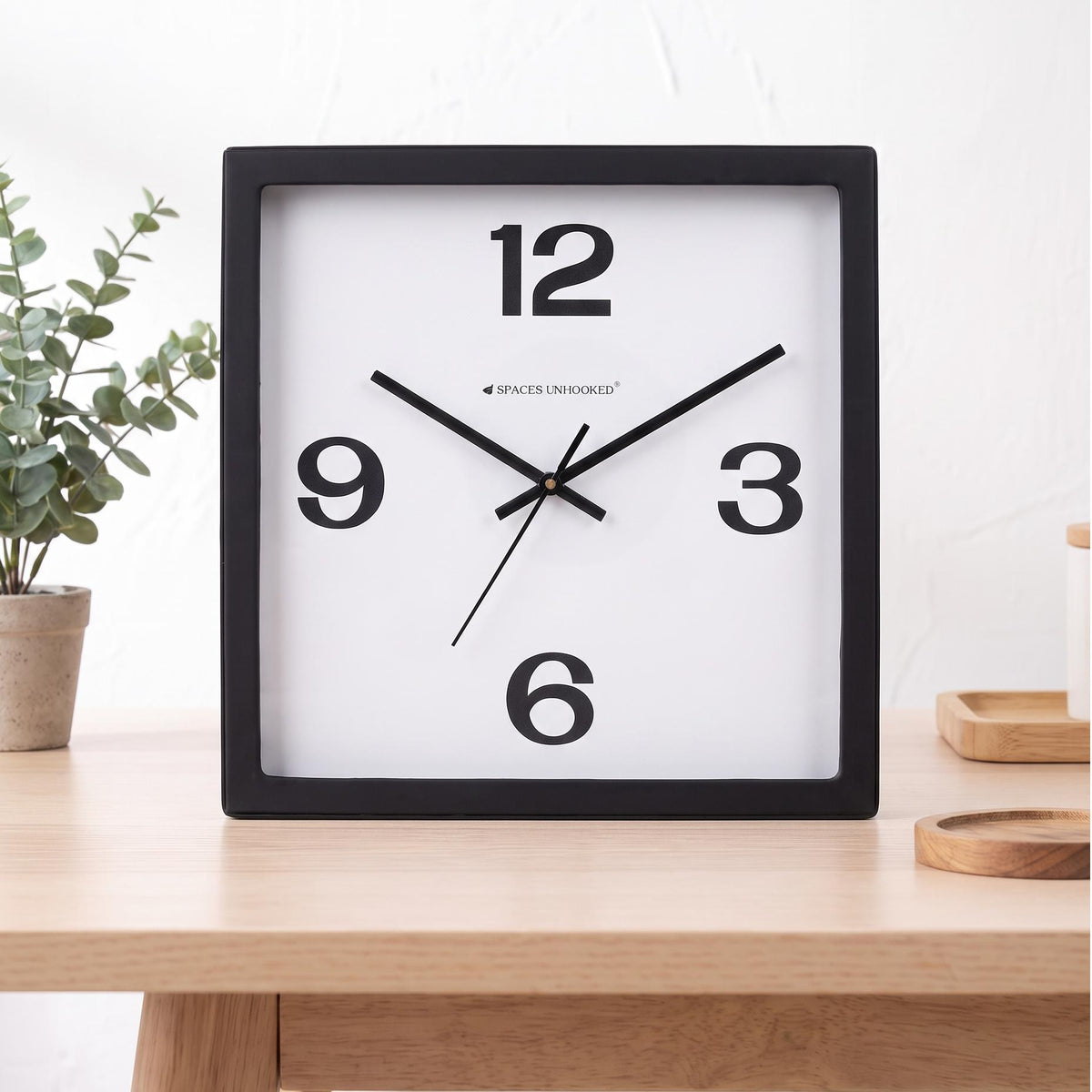 Black square frame and clear cover of a bold 12-3-6-9 wall clock, close-up view