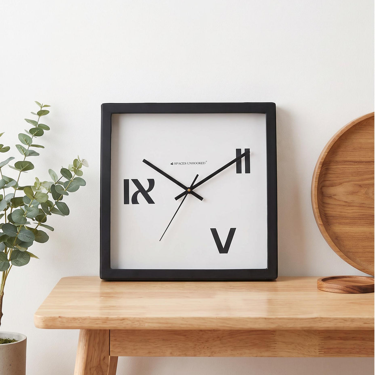 Black square frame and clear cover of a three Roman numeral wall clock, close-up view