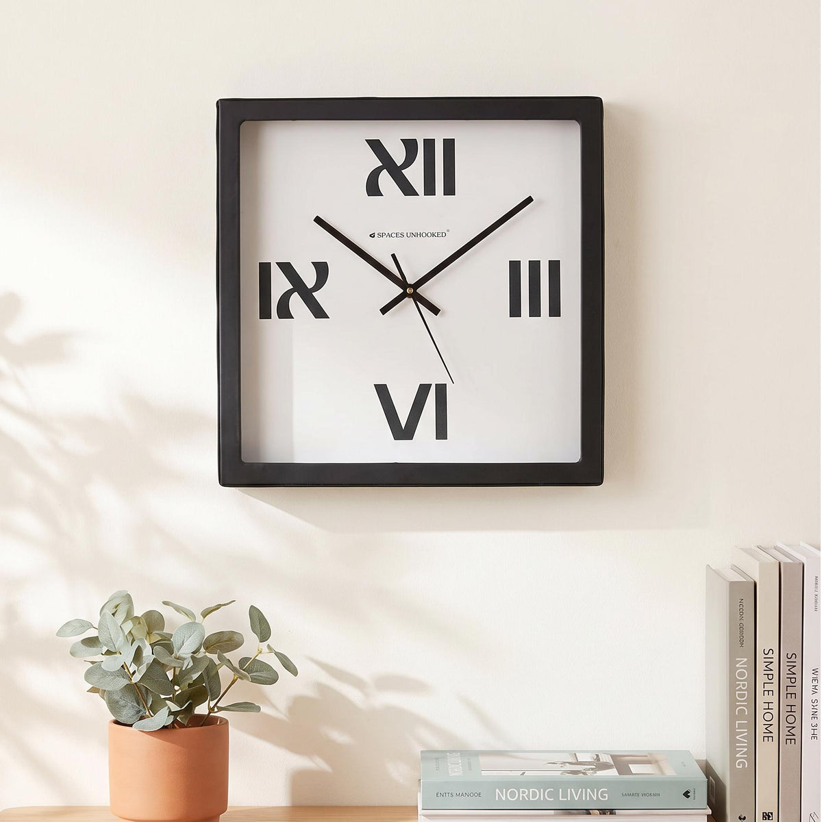 Black square frame and clear cover of a bold Roman numeral wall clock, close-up view