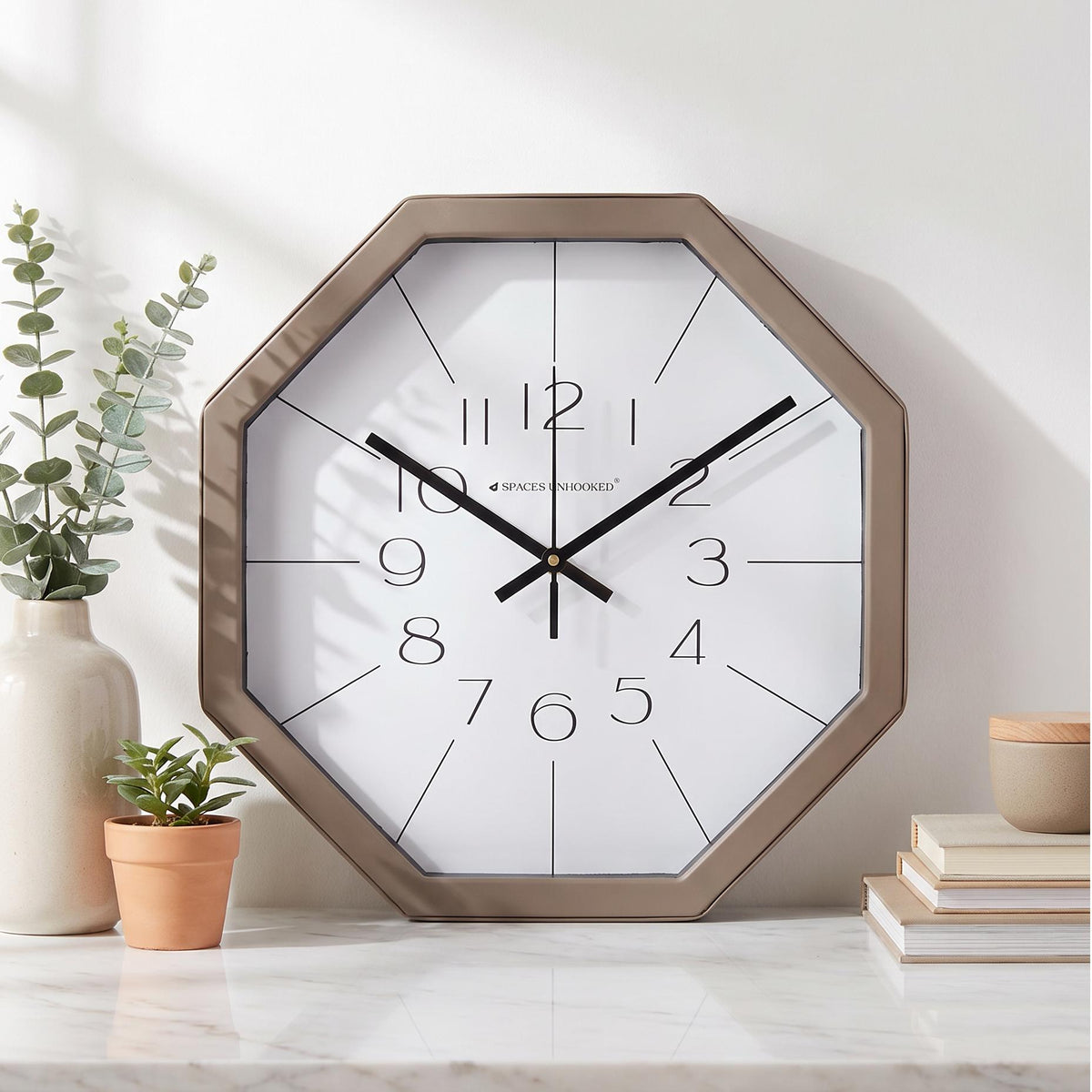Long thin radiating lines dividing the white dial of a taupe octagonal wall clock