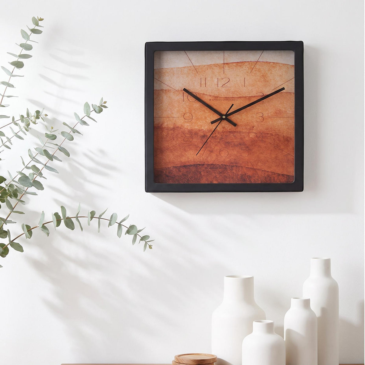 Black square frame and clear cover of a terracotta watercolour wall clock, close-up view