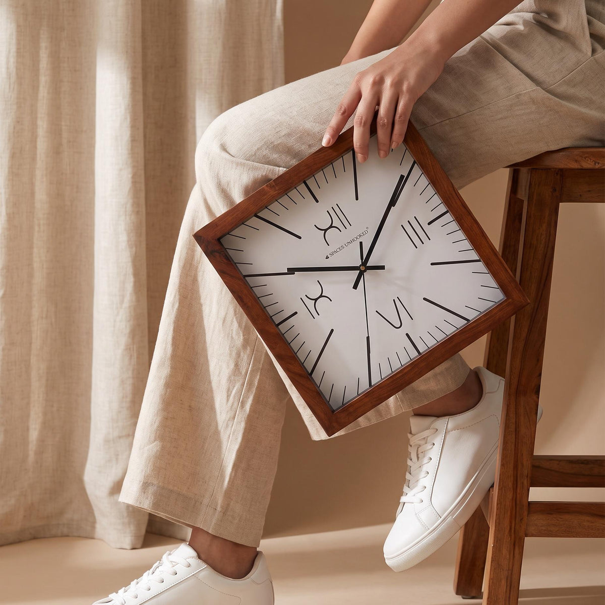 Close-up of slim Roman numerals XII, III, VI and IX on a white square wall clock dial
