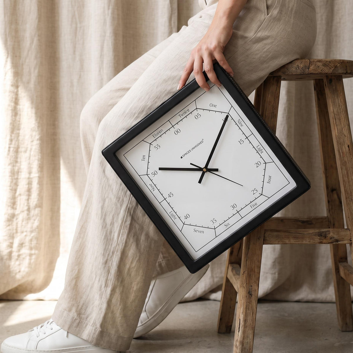 Square black word dial wall clock on a living room wall above a sofa