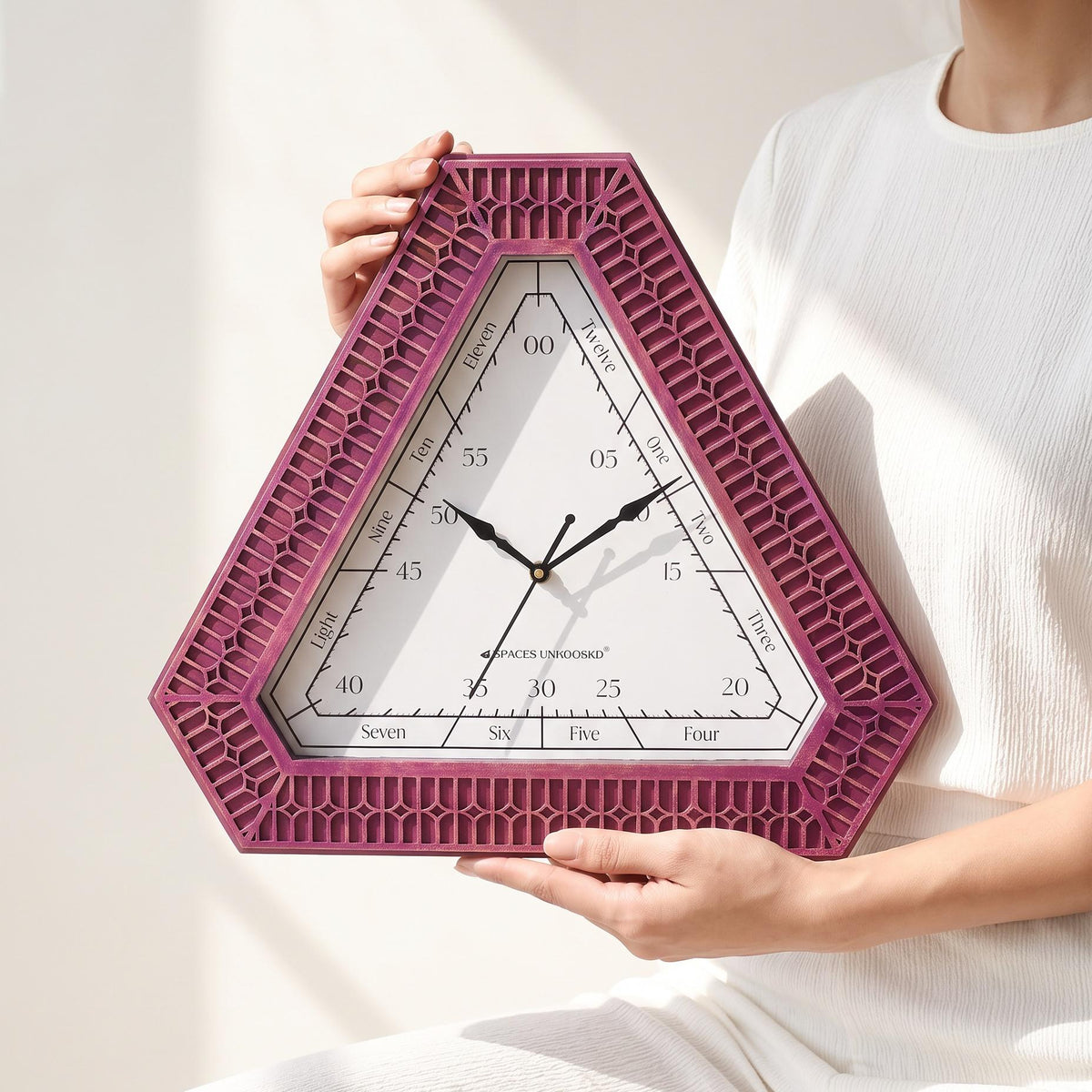 Close-up of hours spelled in words and minutes in fives on a white triangular clock dial