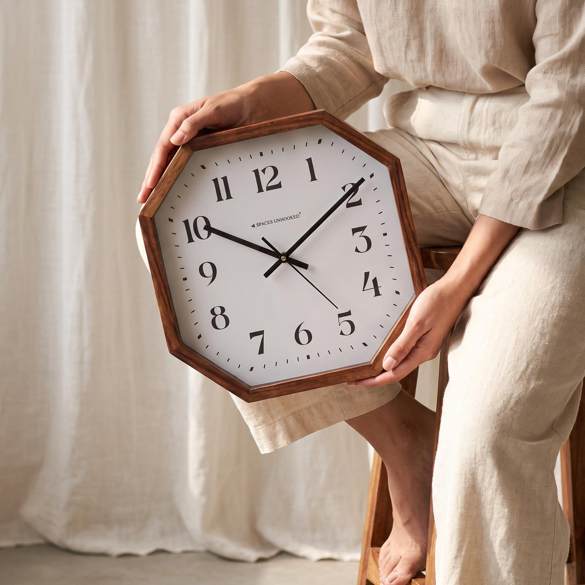 Cut-corner wooden wall clock with classic numerals hanging above a sofa in a bright living room