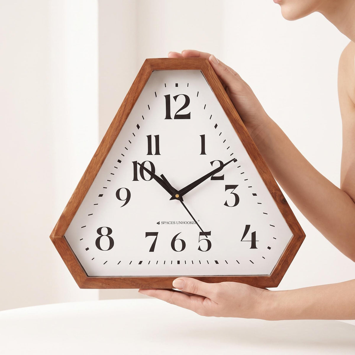Triangular wooden wall clock with classic numerals hanging above a sofa in a bright living room