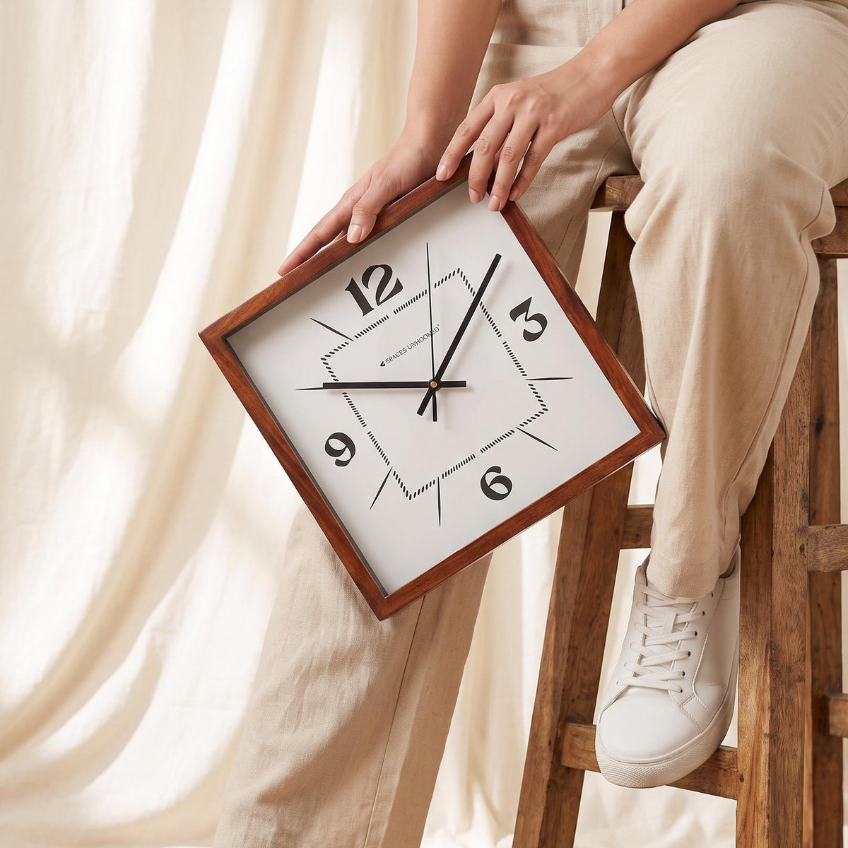Modern square wooden wall clock with dotted dial on a white living room wall above a sideboard