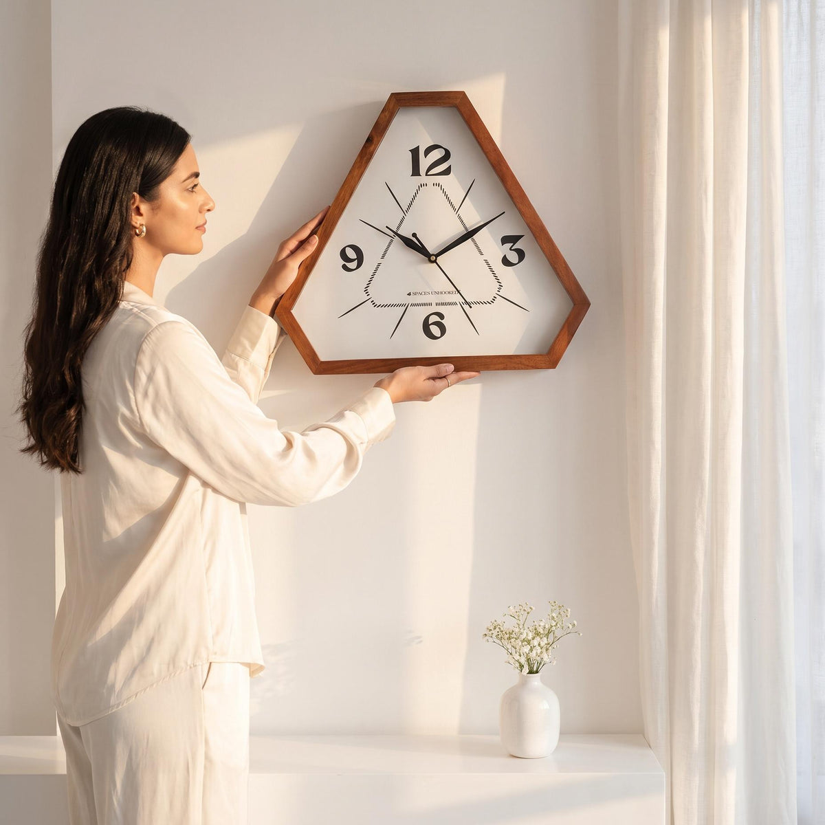 Triangular wooden wall clock with dotted dial on a white wall above a living room sofa