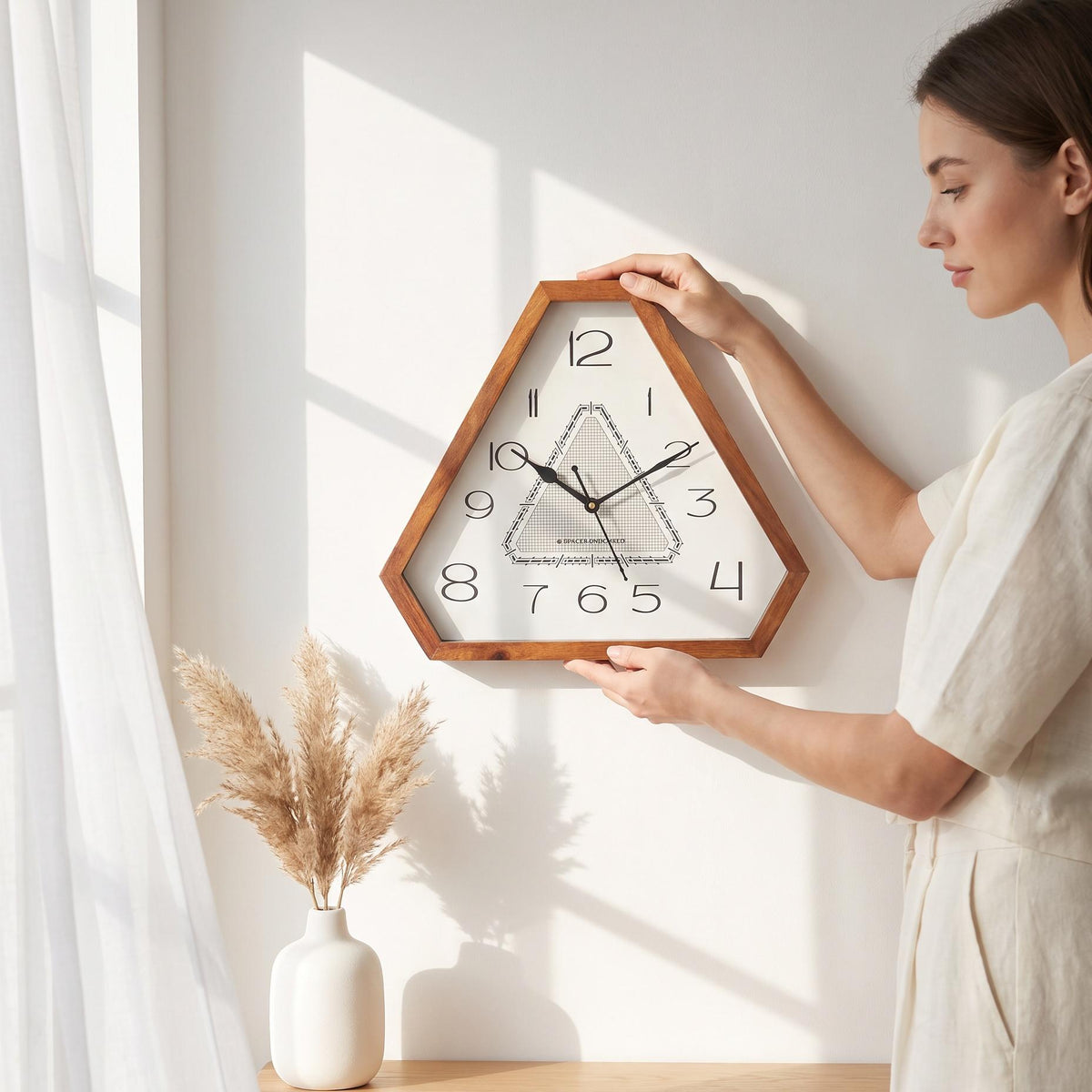 Art deco triangular wooden wall clock on a plain living room wall above a sofa with brass lamps