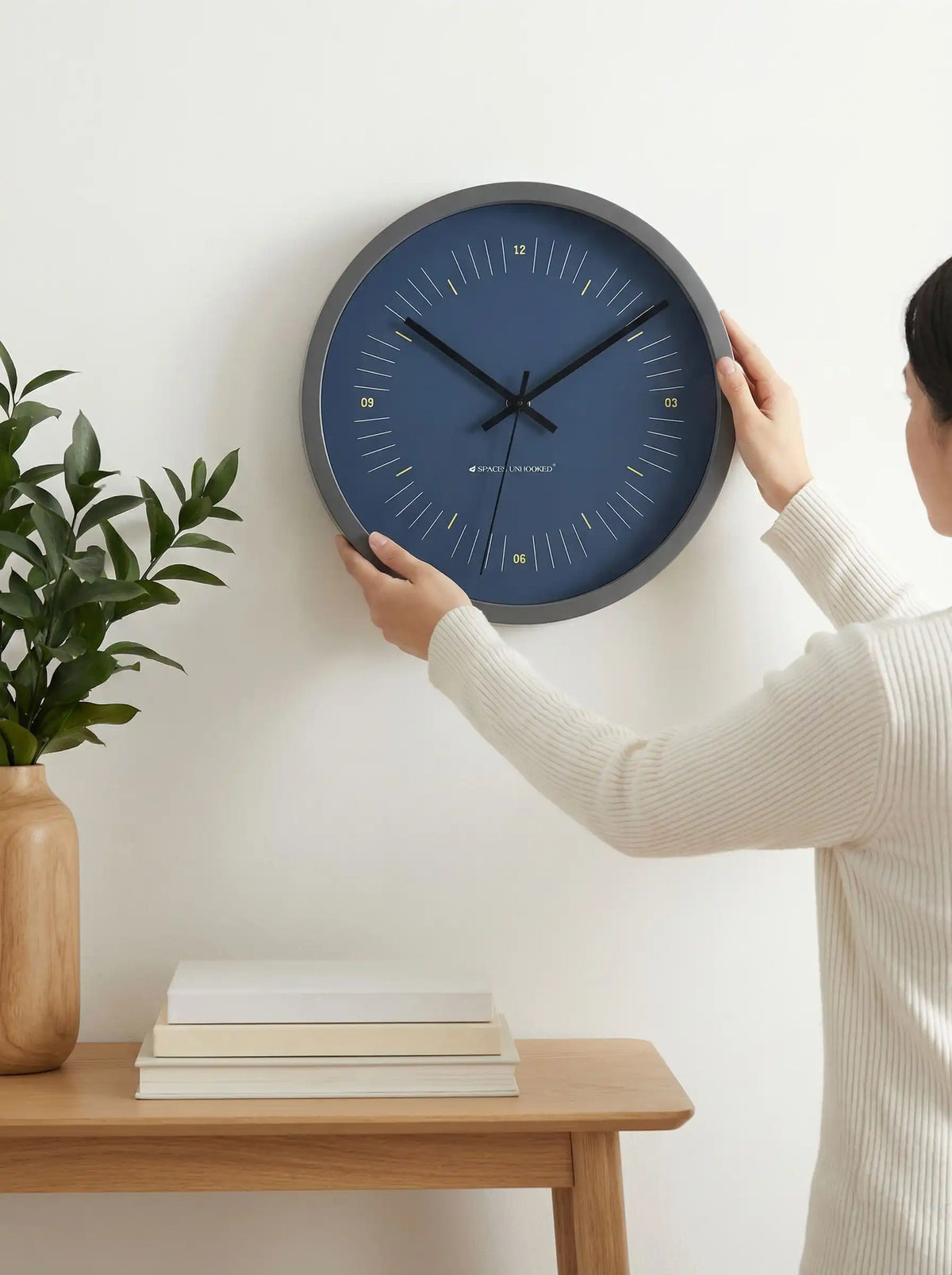 Lifestyle AI – Designer wall clock being mounted on wall by woman in cream sweater