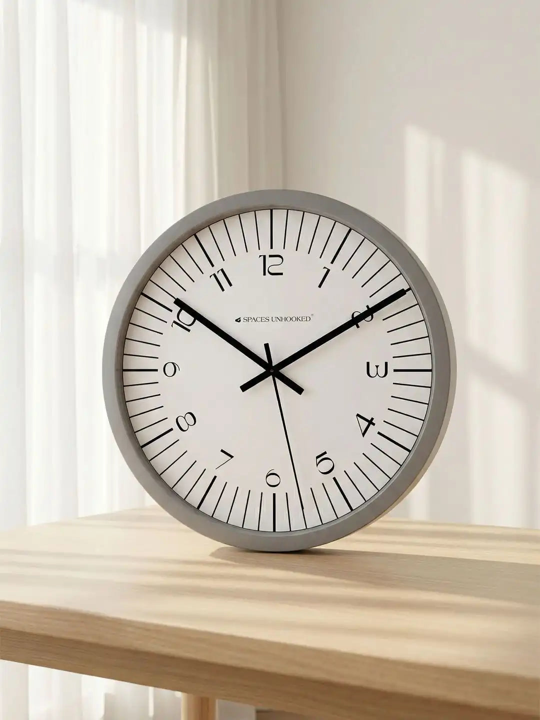 Spaces Unhooked grey minimalist wall clock styled on a wooden tabletop in a bright modern interior