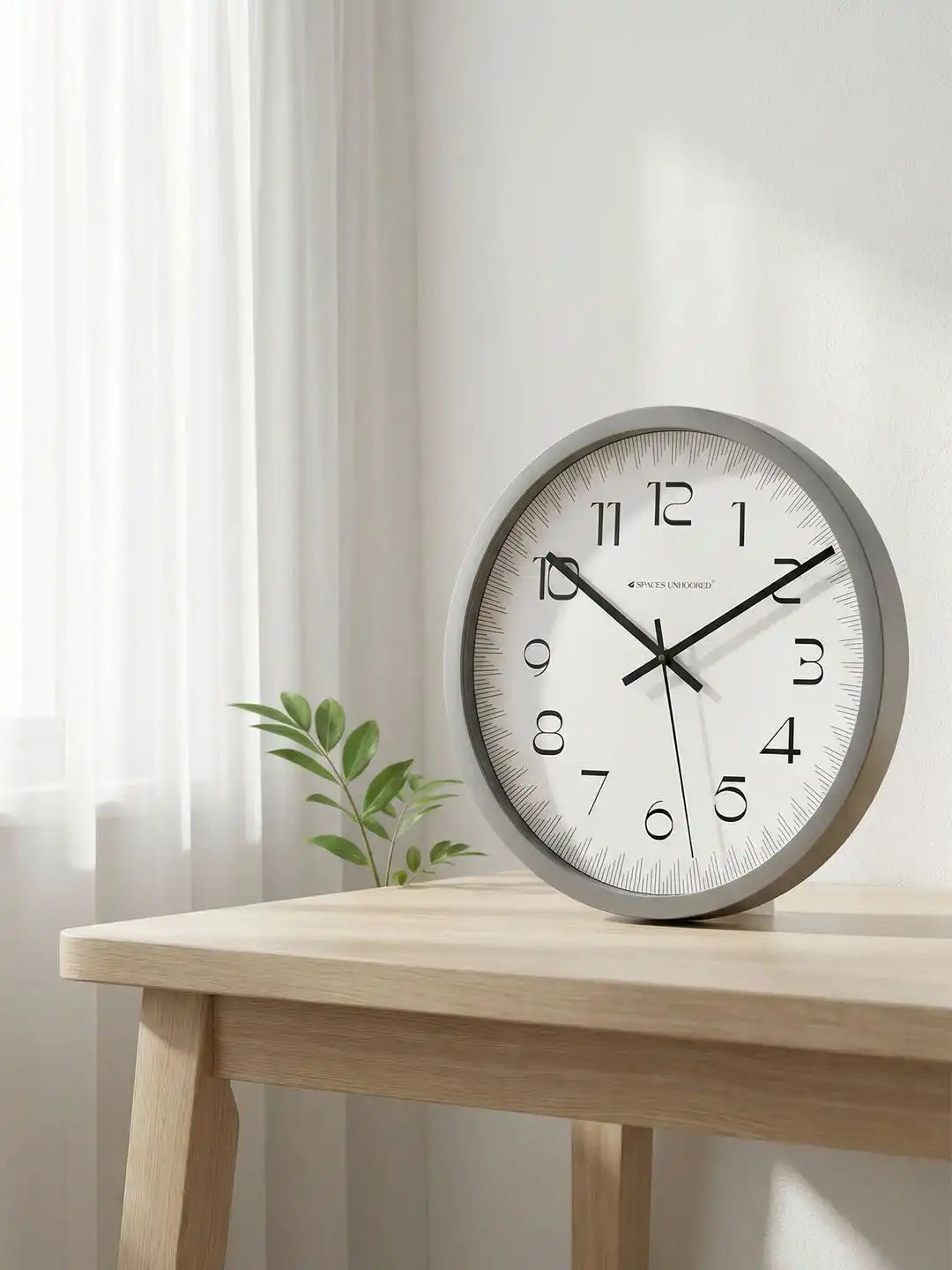 Spaces Unhooked grey wall clock styled on a wooden table in a bright contemporary home interior