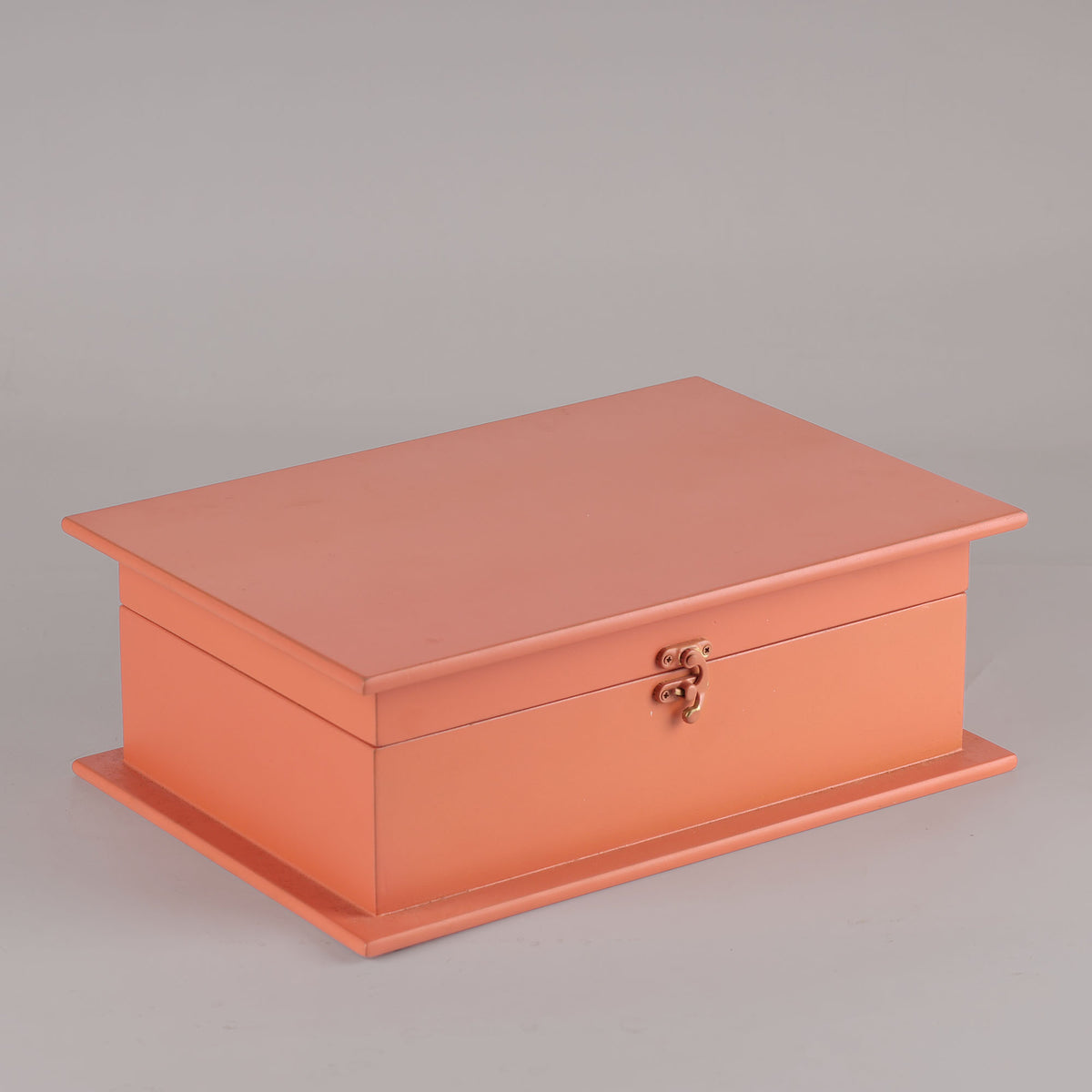 Coral-colored jewelry box with a gold clasp on a gray background